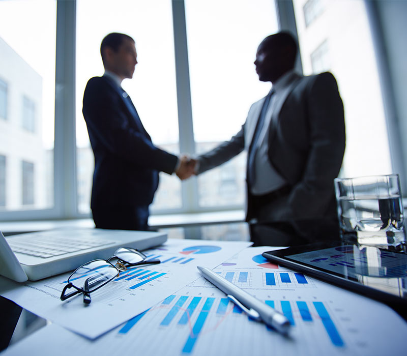 two men shaking hands in office building looking over the city